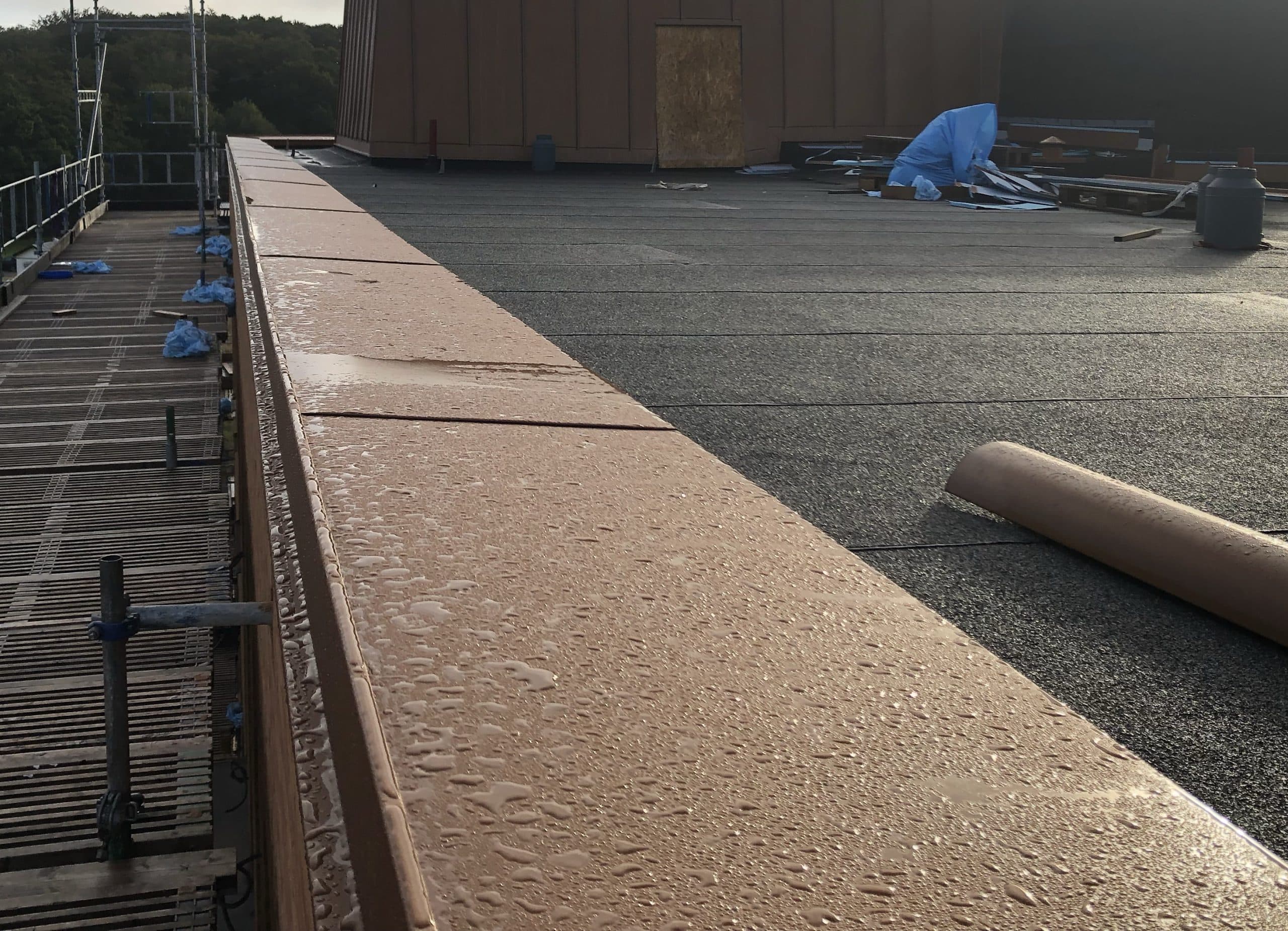 Krönbeslag monterat längs en betongmur på ett tak