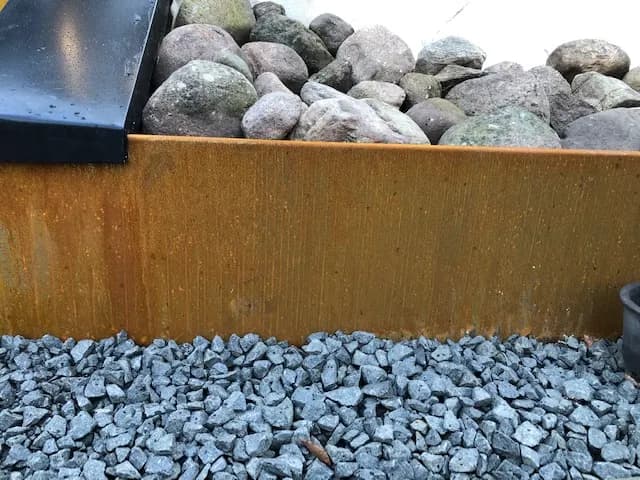 Cortenlåda fylld med natursten, omgiven av singel. Bild 5 av 22
