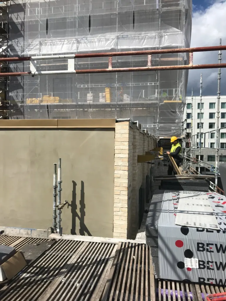 Plåtslagare arbetar på ett tak mellan byggnaden och ställningen. Bild 1 av 6