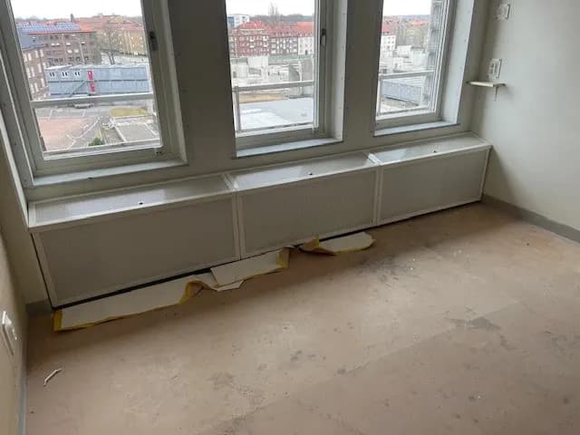 Låga elementskydd i vit plåt under en fönsterrad. Bild 1 av 7