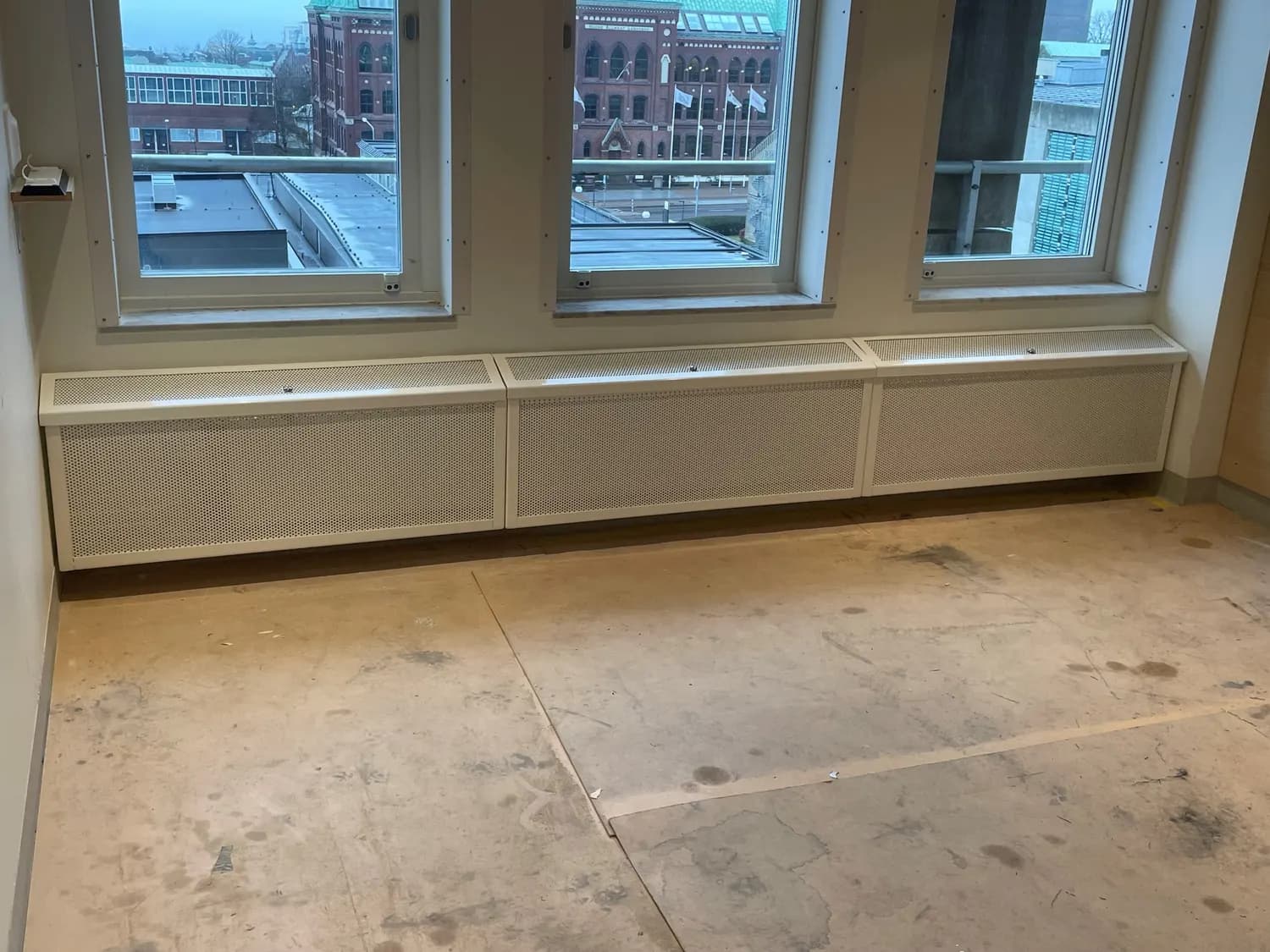 Rad av elementskydd under fönstren i ett rum med utsikt över staden. Bild 5 av 7