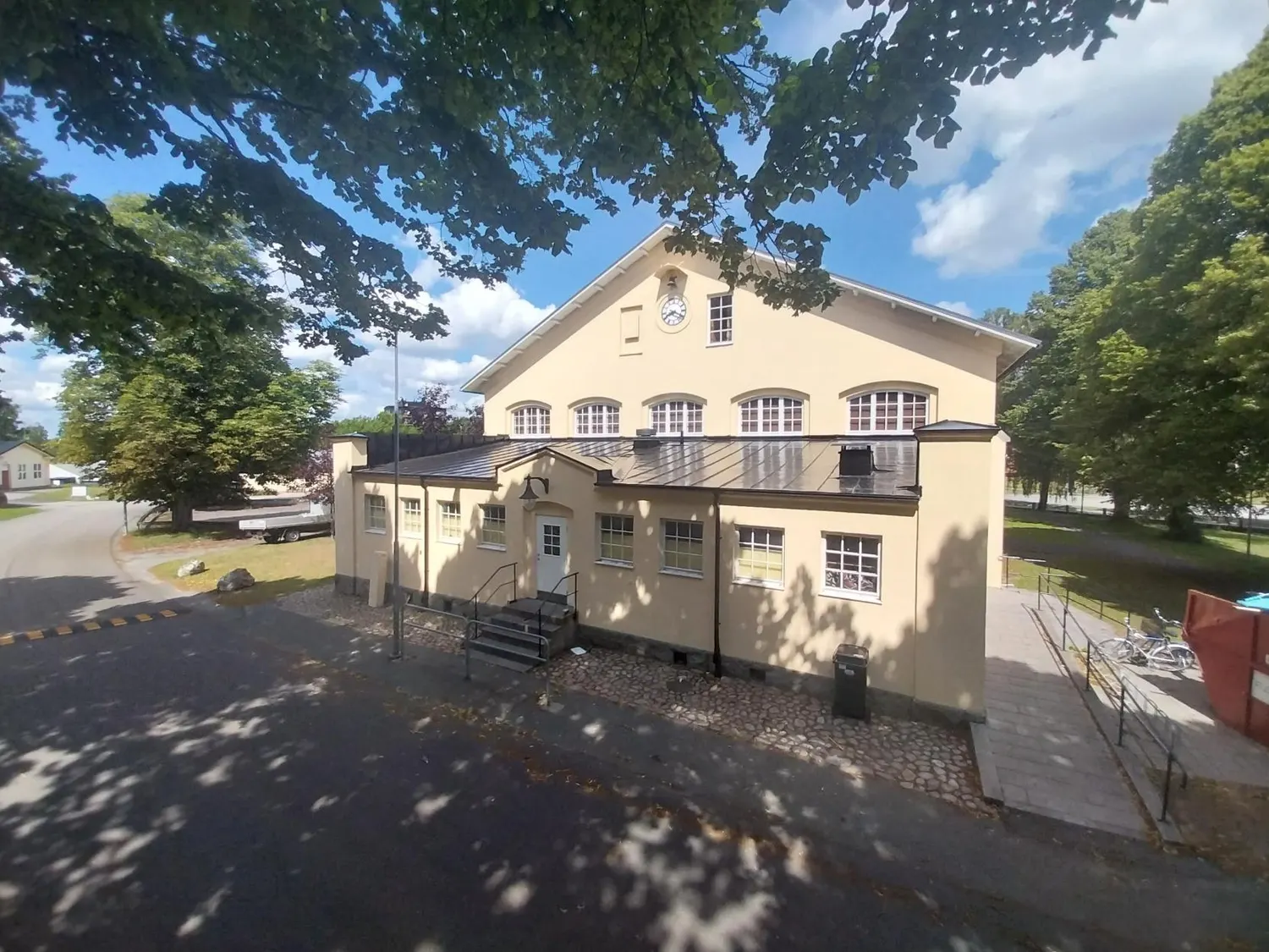 Gulputsad byggnad med nytt mörkt tak, sedd genom lövverk. Bild 11 av 62