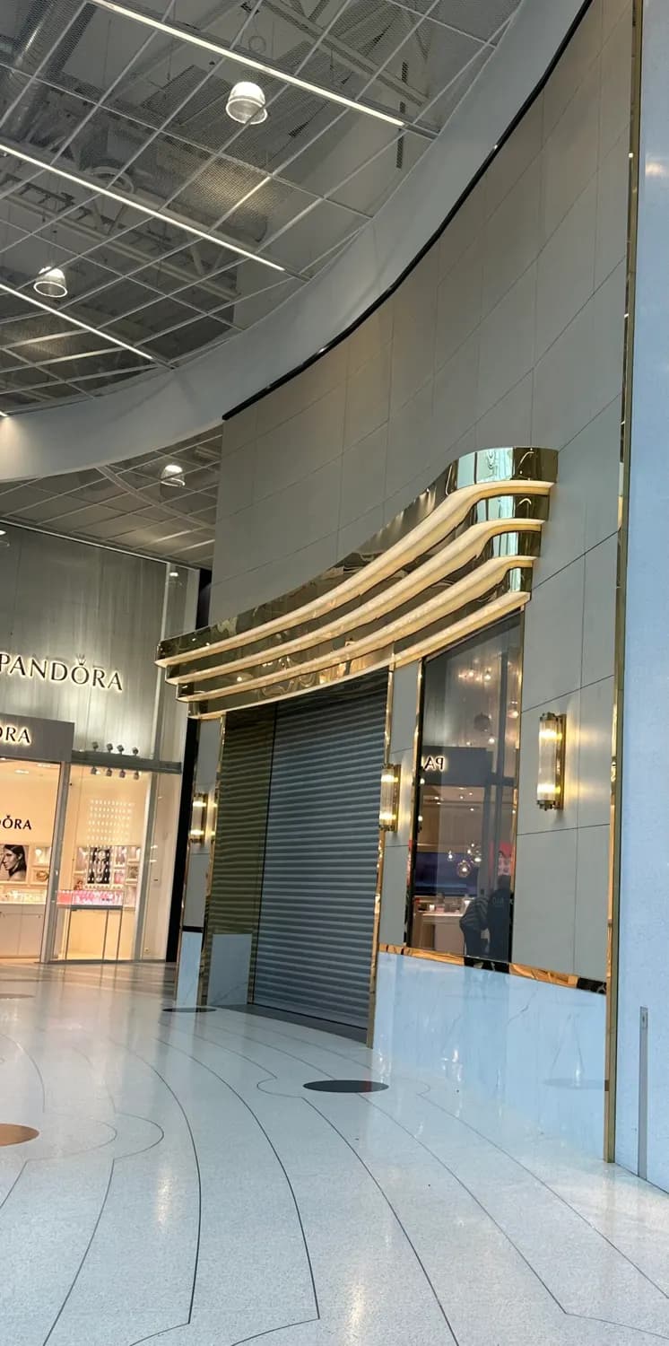 Butiksfasad med svängda lister i guldfärgat rostfritt över entrén. Bild 1 av 8