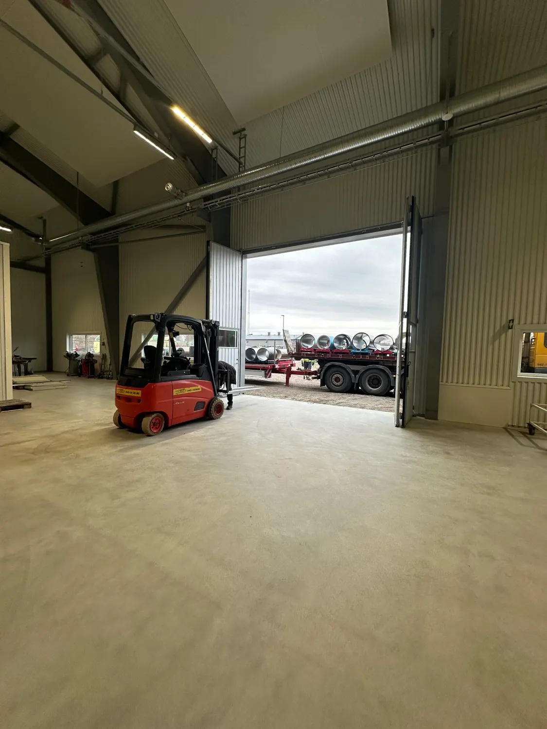 Truck i hallen vid öppen port, med material på släp utanför. Bild 12 av 16