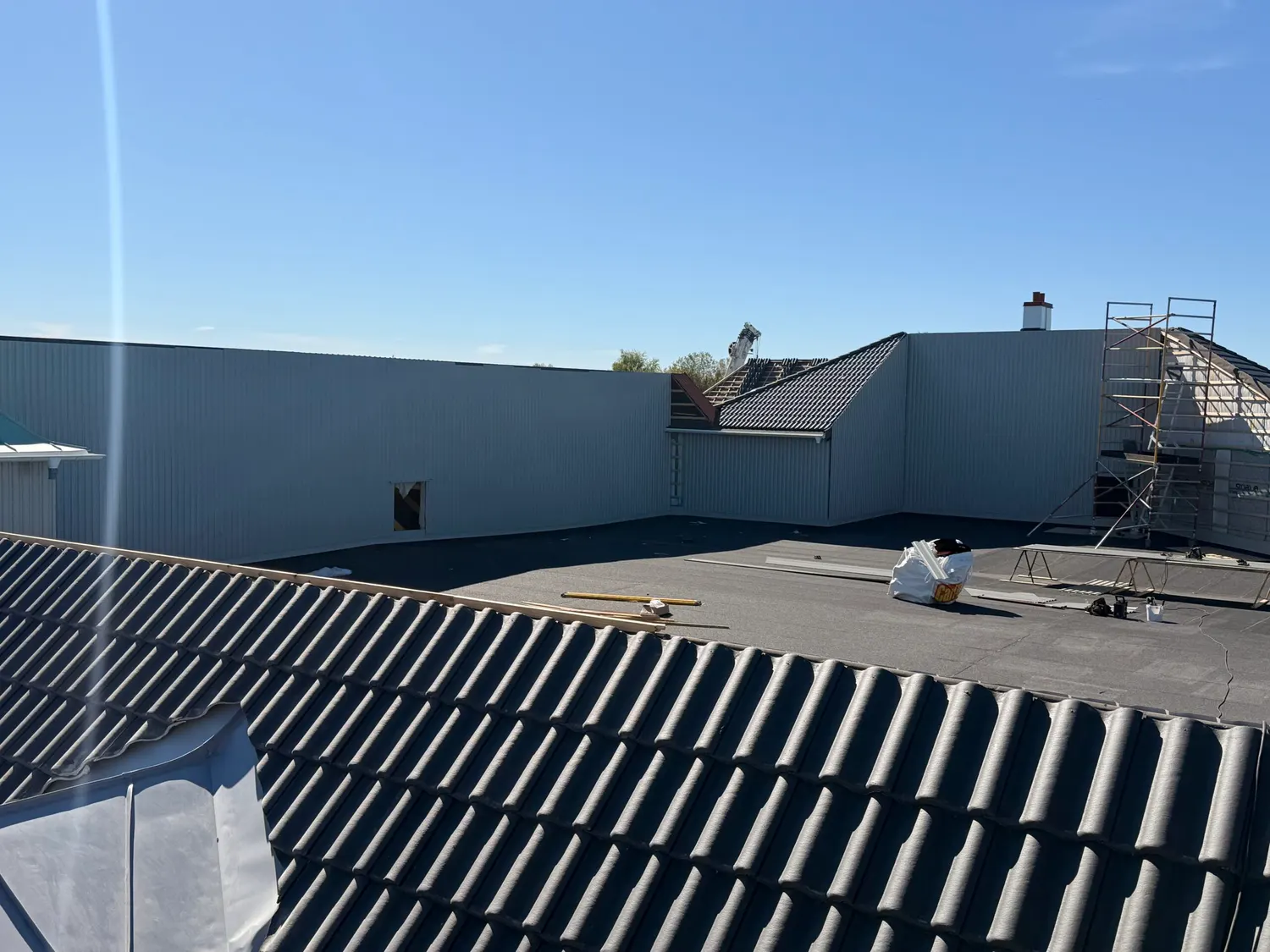 Svart taktegel i förgrunden mot vita fasadskivor på nästa byggnadskropp. Bild 4 av 4