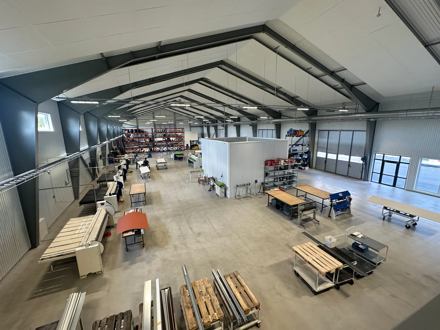 Verkstadshallen inifrån med takstolar, arbetsbänkar och materialhyllor. Bild 4 av 16