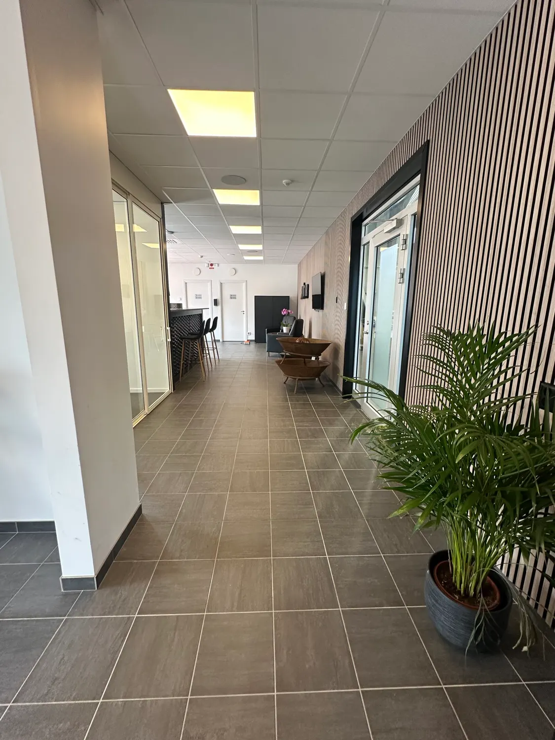 Korridor genom kontorsdelen med klinkergolv och glasade kontorsrum. Bild 8 av 16