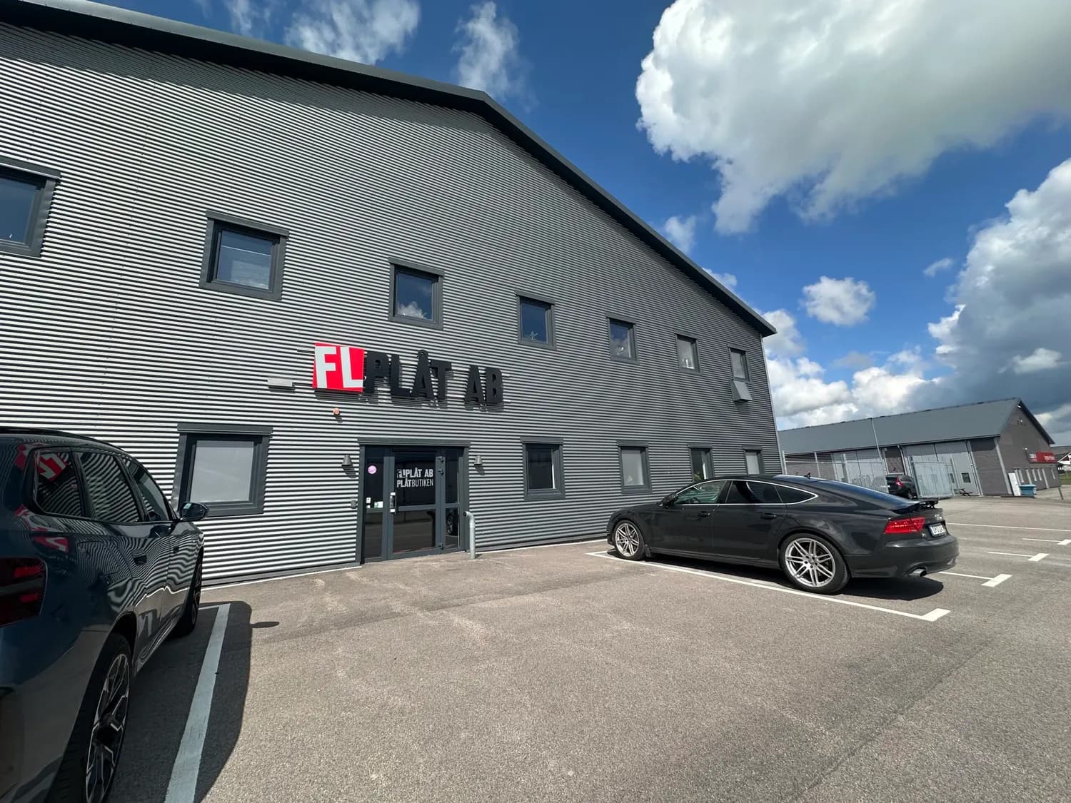 Nya lokalens fasad i grå profilerad plåt med företagsskylten på gaveln. Bild 1 av 16