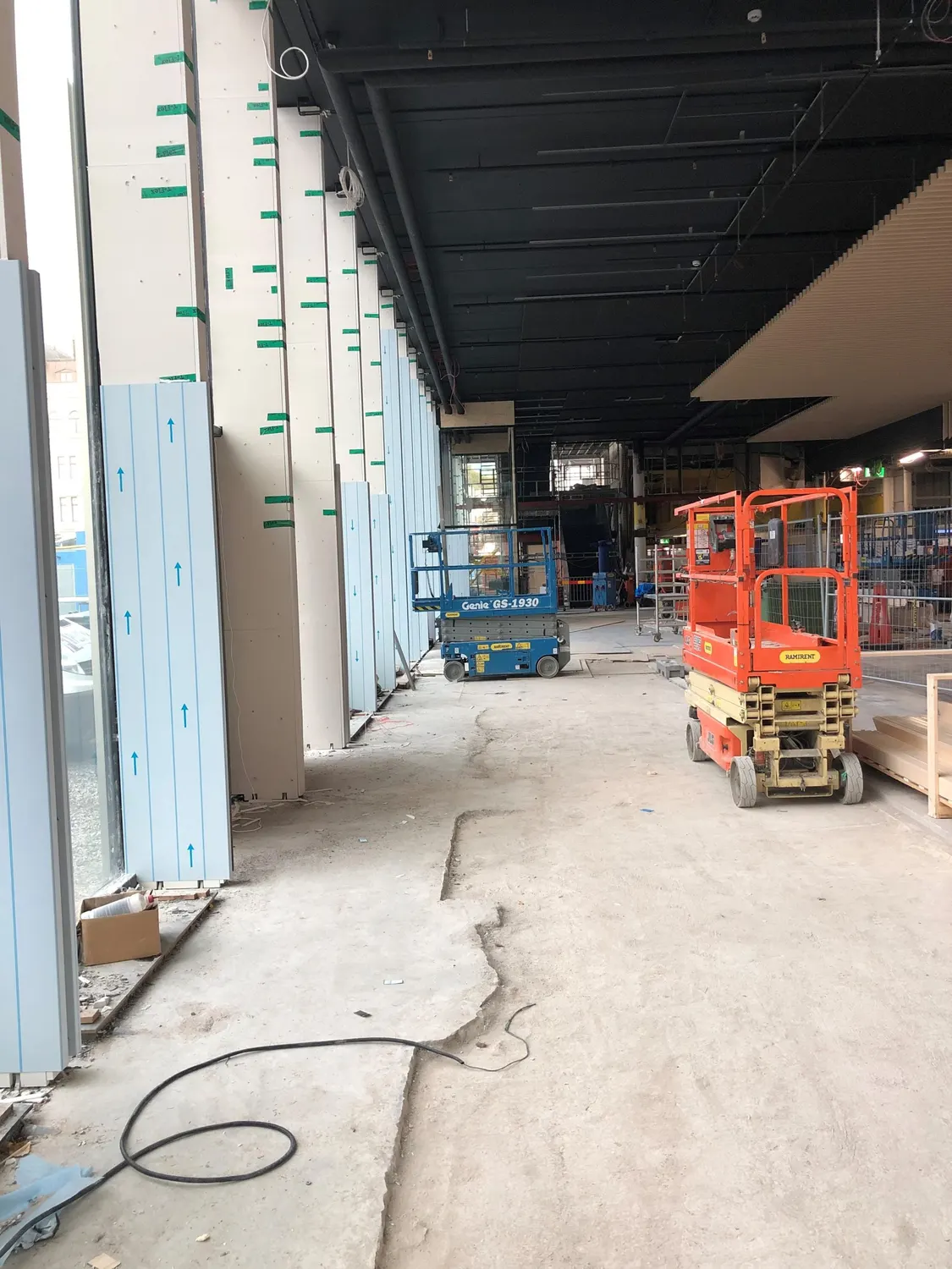 Byggnadens insida under montering, med saxlift och material. Bild 8 av 14
