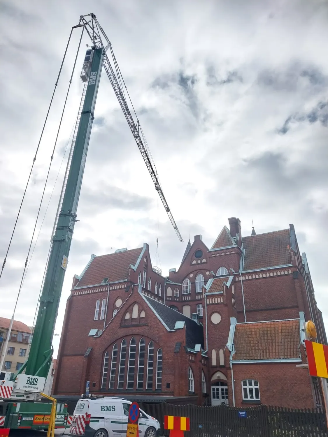 Kranens arm sträckt över skolans tak under arbetet. Bild 2 av 2