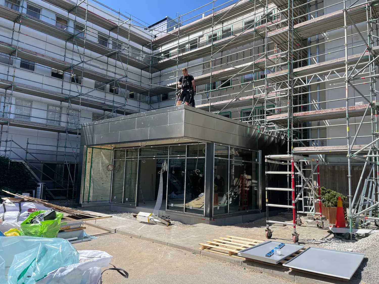 Entré med skärmtak klätt i mattslipad rostfri plåt, byggnadsställning runt fasaden. Bild 1 av 5