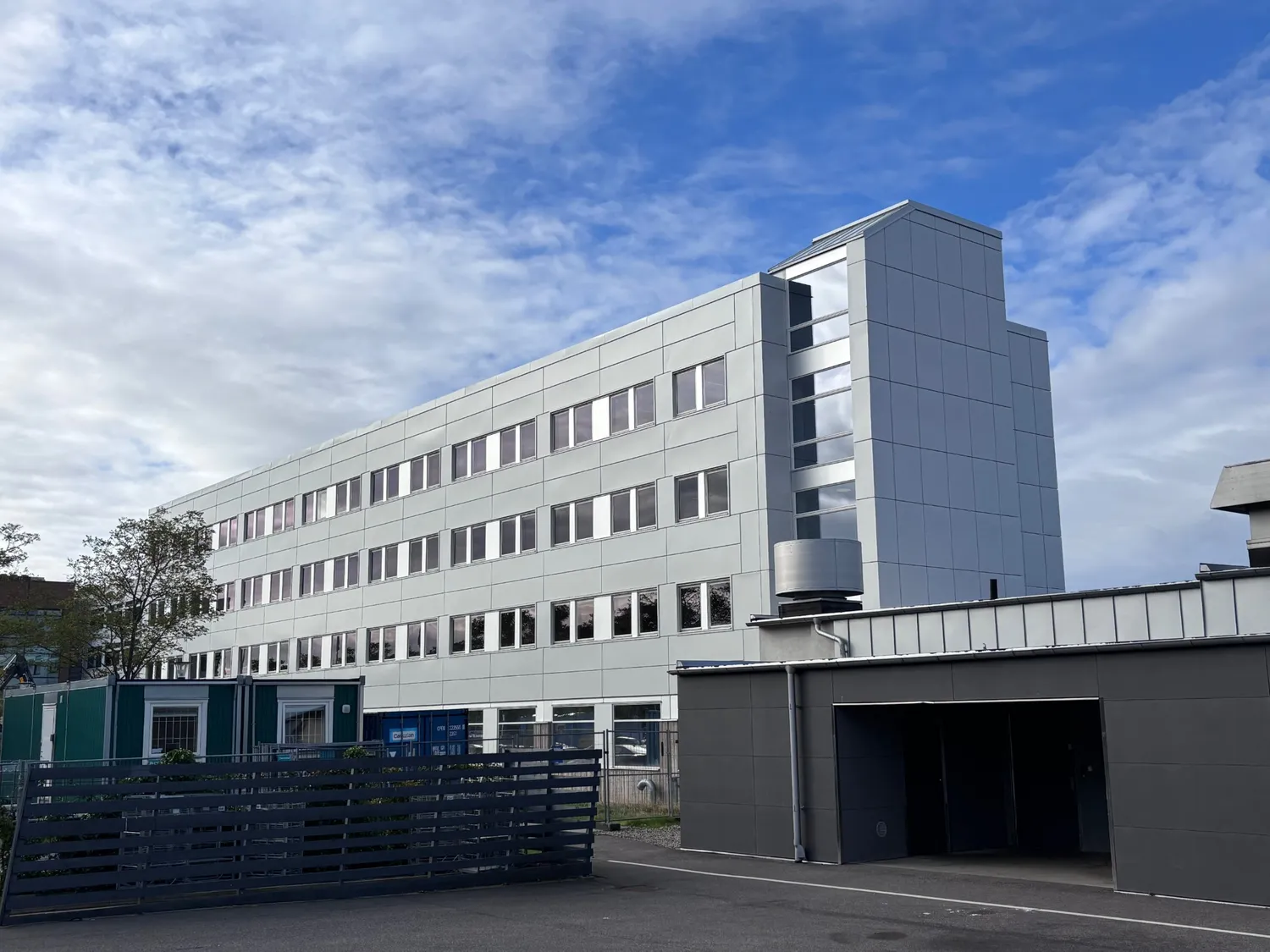 Den färdiga byggnaden sedd från sidan, med ett uppglasat trapptorn och en vinklad takfot i plåt, samt ett plåtklätt garage i förgrunden. Bild 11 av 11