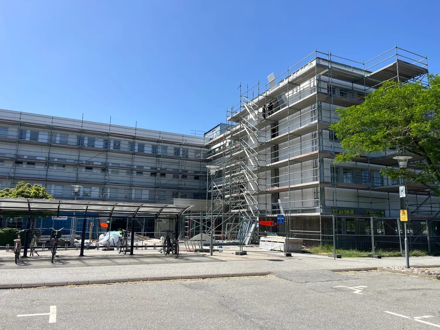 Långsidan med ställning längs hela fasaden och entrén till vänster. Bild 4 av 5