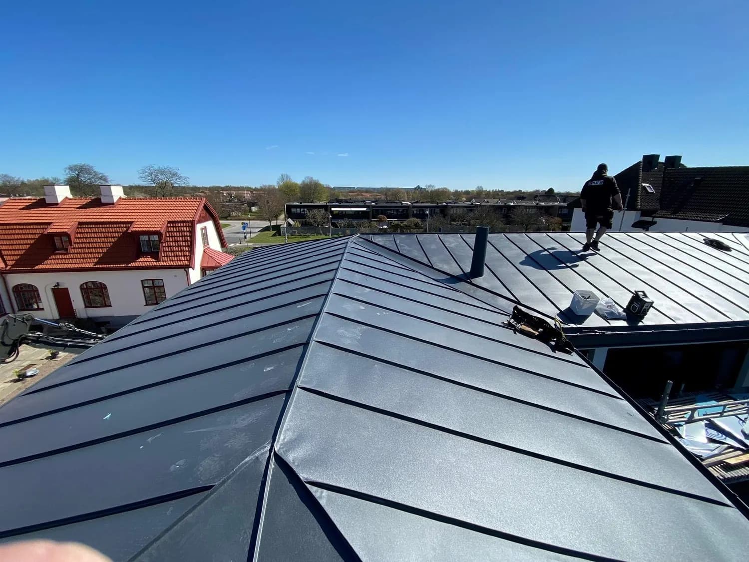 Valmat tak i mörk plåt med ventilhuvar längs nocken. Bild 18 av 62