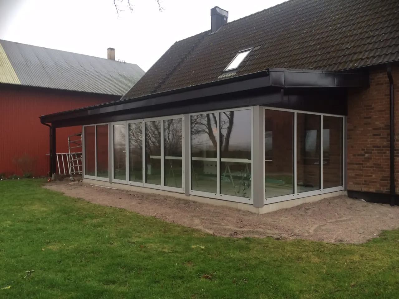 Inglasat uterum med plåttak intill en röd träfasad. Bild 32 av 62