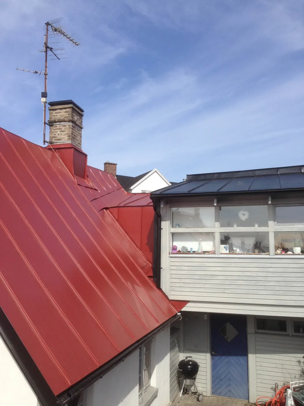 Rött plåttak över flera takfall, med skorsten i tegel. Bild 35 av 62