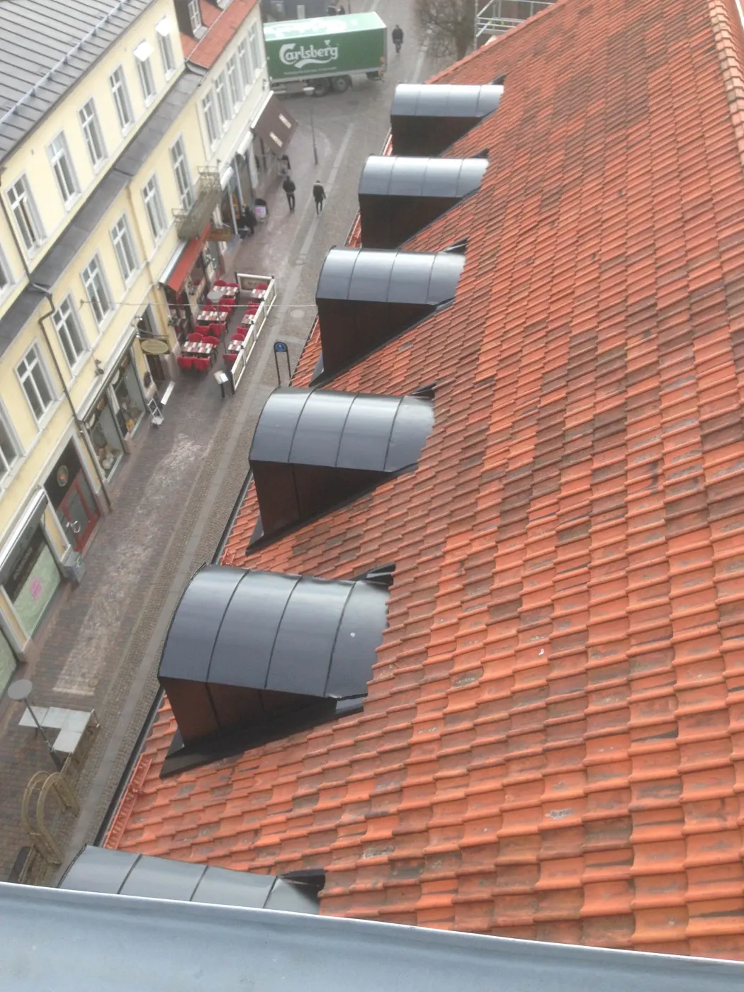 Tegeltak med rad av plåtklädda ventilhuvar, gatan nedanför. Bild 37 av 62
