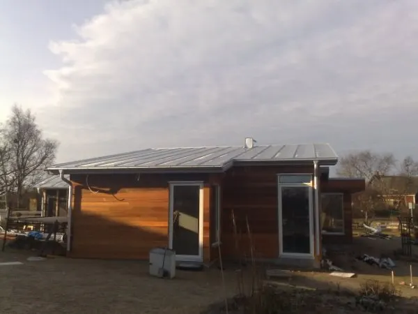 Trähus med ljust plåttak i motljus, gaveln mot kameran. Bild 39 av 62