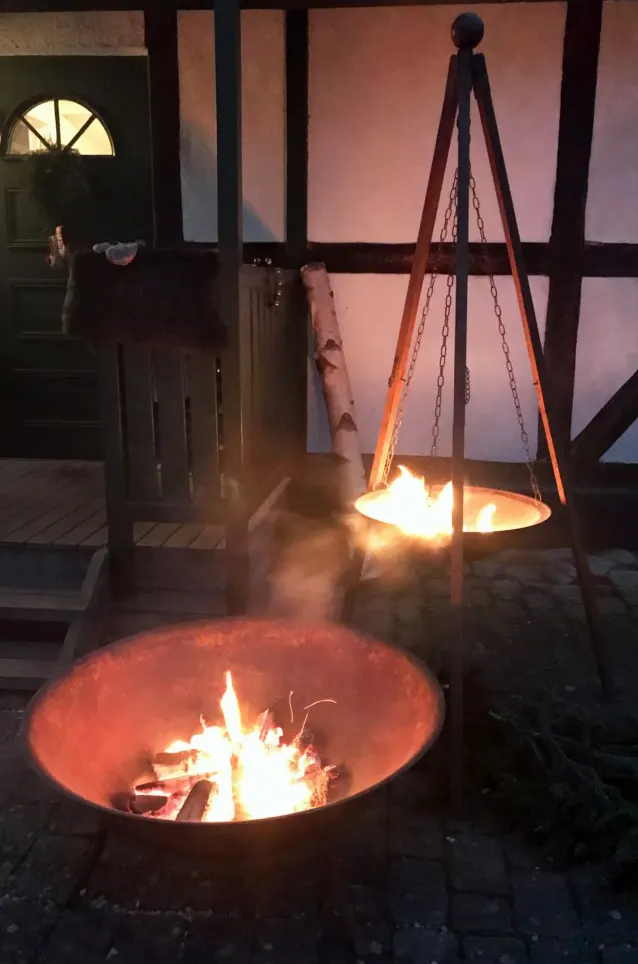 Eldfat med brasa och hängande gryta över elden i skymningen. Bild 22 av 22