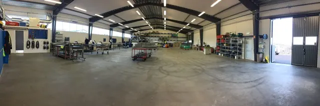 Verkstadshallen inifrån med takstolar och belysning tänd. Bild 22 av 23