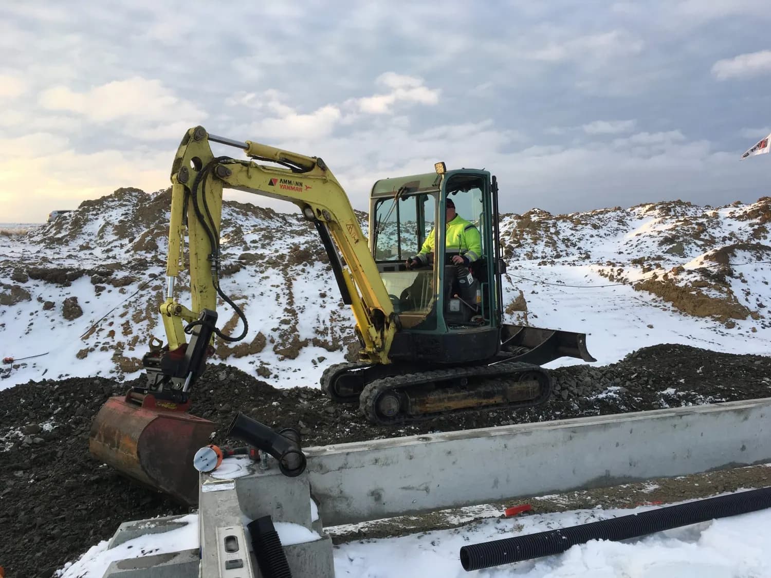 Grävmaskin i snön intill de gjutna sockelelementen. Bild 9 av 23