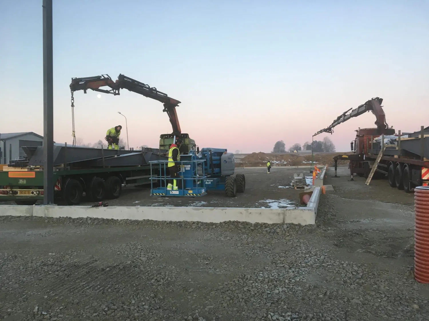 Stålpelare lossas från lastbil i soluppgången. Bild 10 av 23