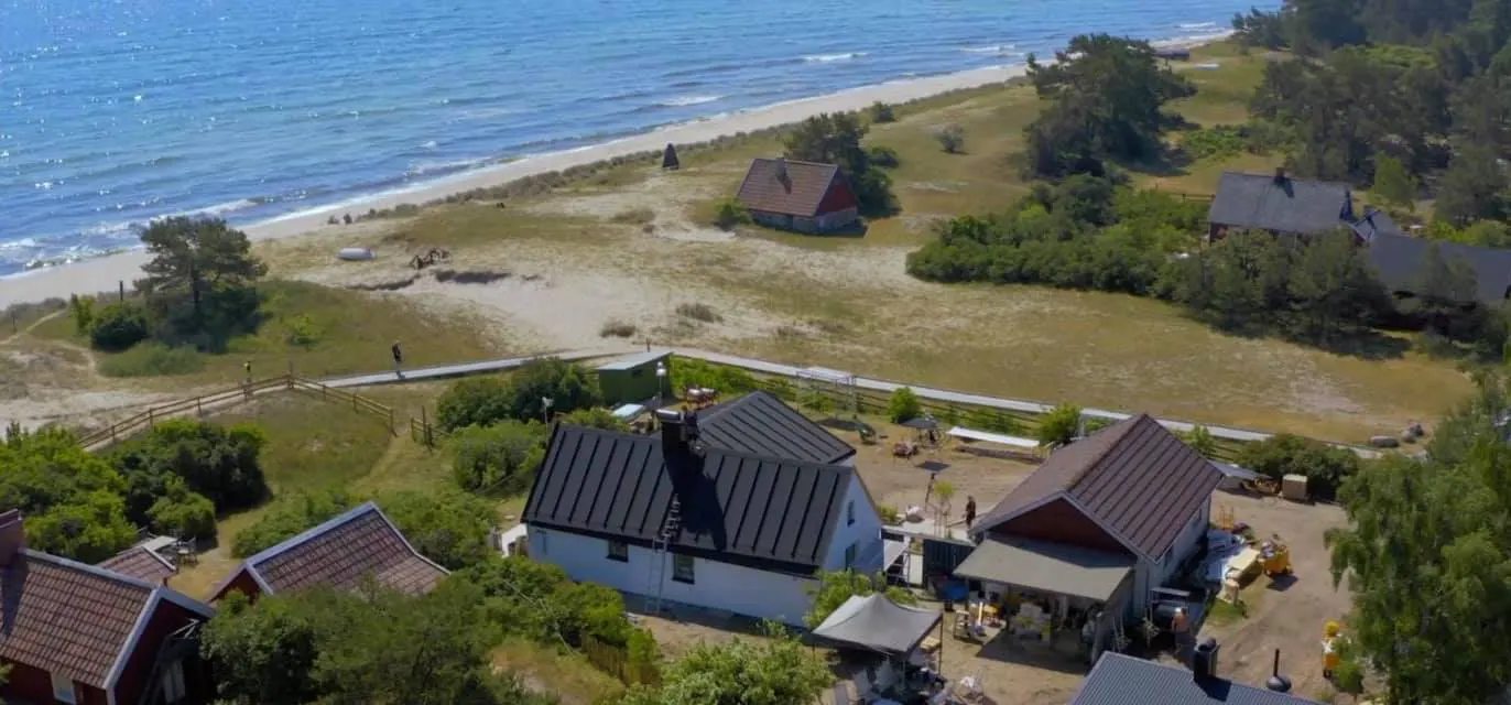 Sommarhuset från luften, med nytt mörkt plåttak och havet bakom. Bild 2 av 4