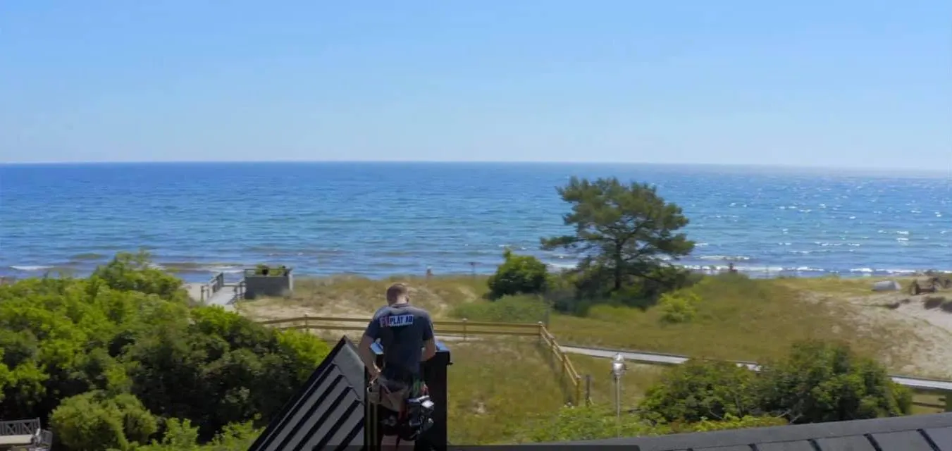 Plåtslagare på taket med utsikt över strand och hav. Bild 4 av 4