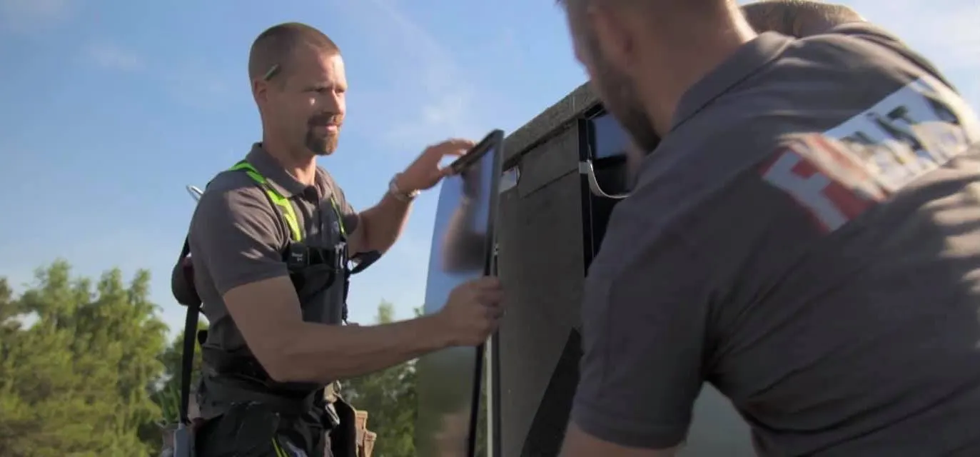 Två personer passar in en mörk plåtskiva på husets vägg. Bild 3 av 4