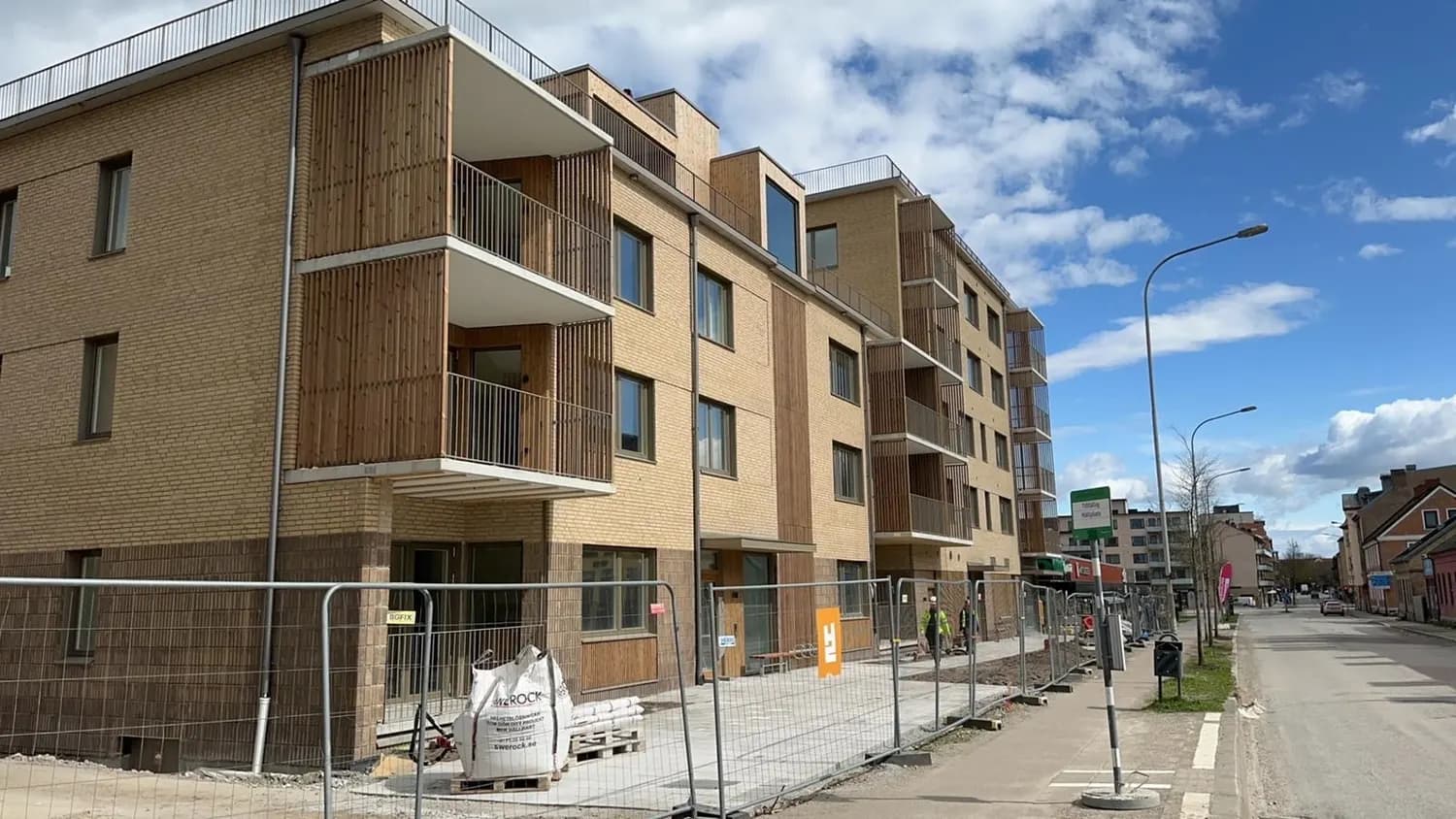 Bostadshusets gatufasad i gult tegel med balkonger och träpartier. Bild 1 av 6