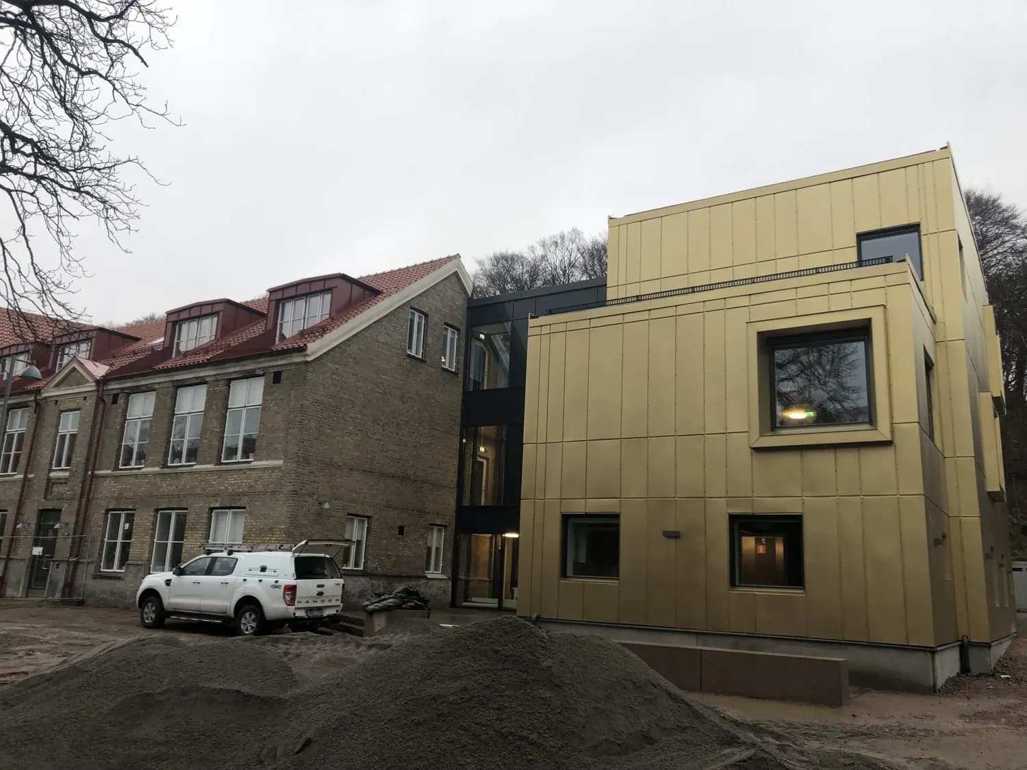 Tillbyggnaden bakom den äldre tegelskolan över en grusad gård. Bild 5 av 11