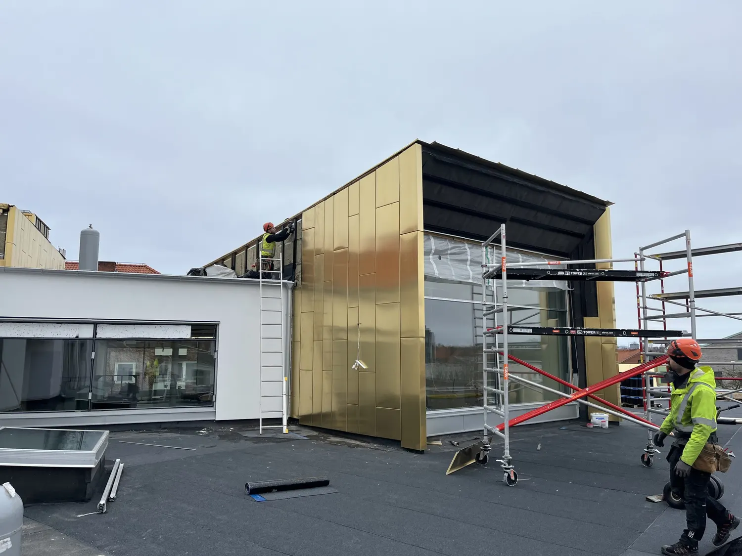 Plåtslagare på stege monterar mässingsfärgade kopparskivor på gaveln. Bild 1 av 21