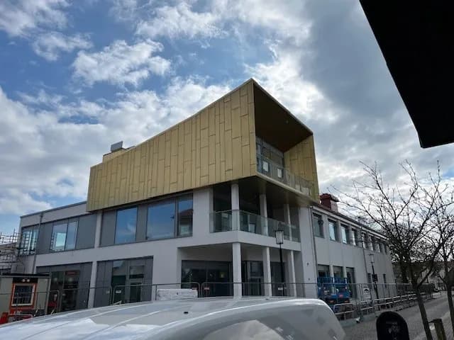 Byggnadens hörn med kopparvolymen kragande ut över entréplanet. Bild 16 av 21