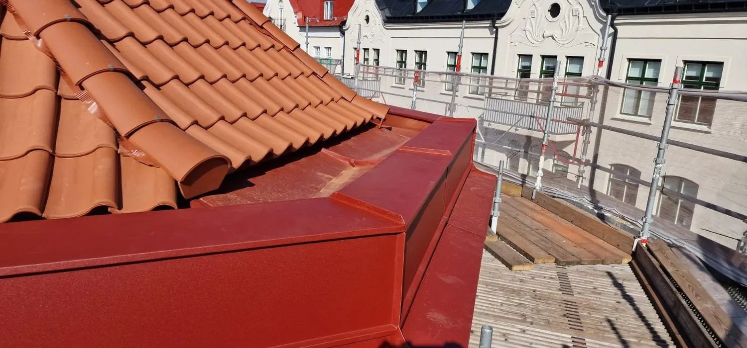 Närbild på nockbeslag i mörkröd plåt där två takfall möts. Bild 5 av 6
