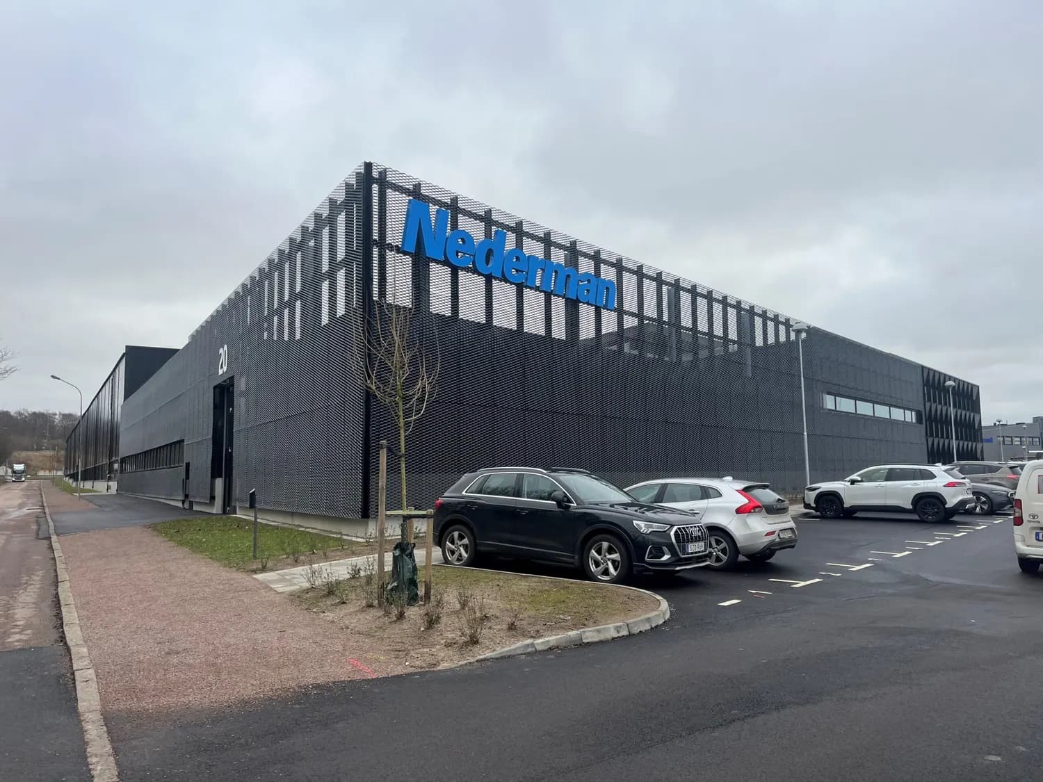 Kontorsbyggnadens hörn i svart plåt med kundens skylt högst upp. Bild 1 av 20