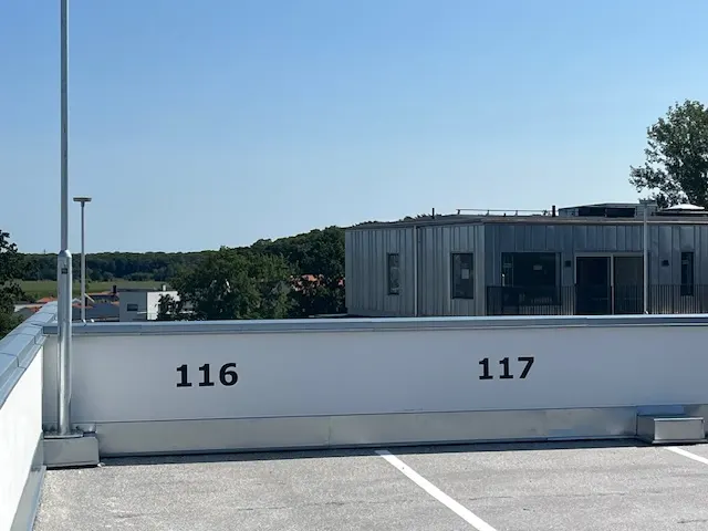 Byggnadens plåtklädda överdel sedd över parkeringsdäckets kant. Bild 4 av 13