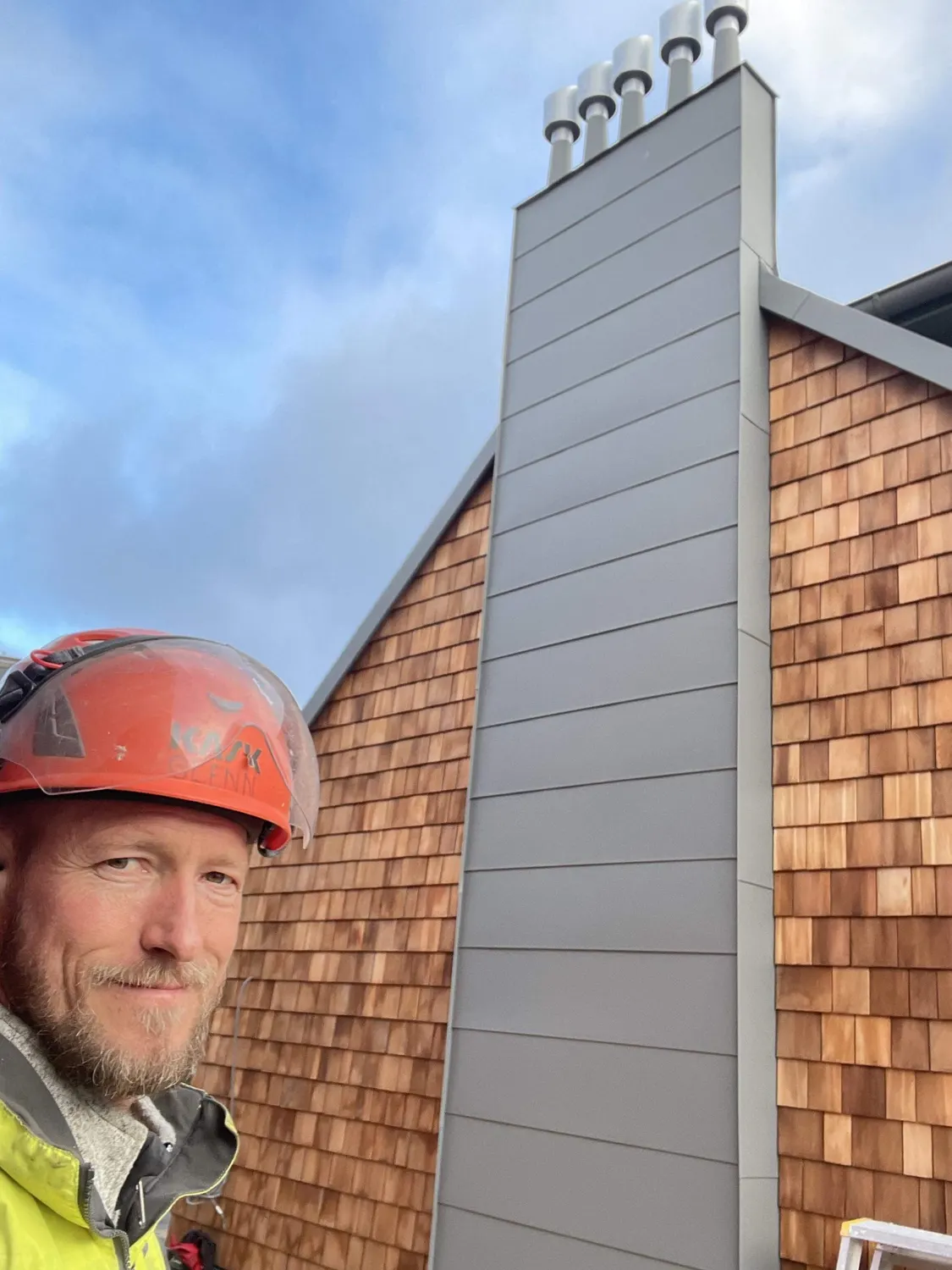 Plåtslagare i hjälm framför gavelns träspån och plåtklädda kant. Bild 3 av 23