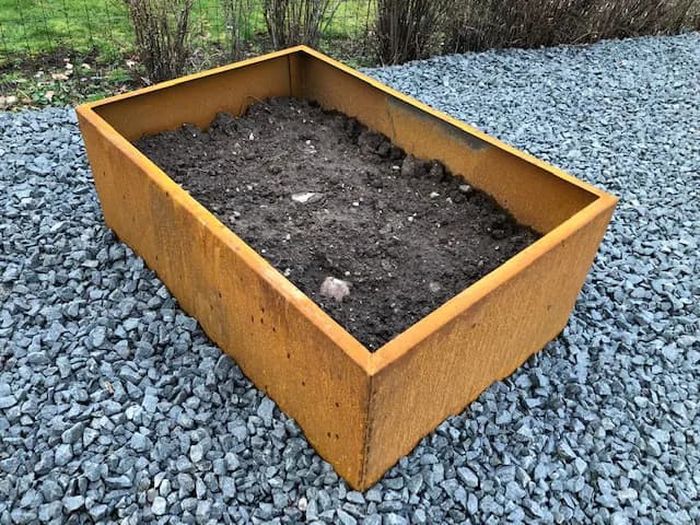 Odlingslåda i corten fylld med jord, stående på singel. Bild 11 av 22