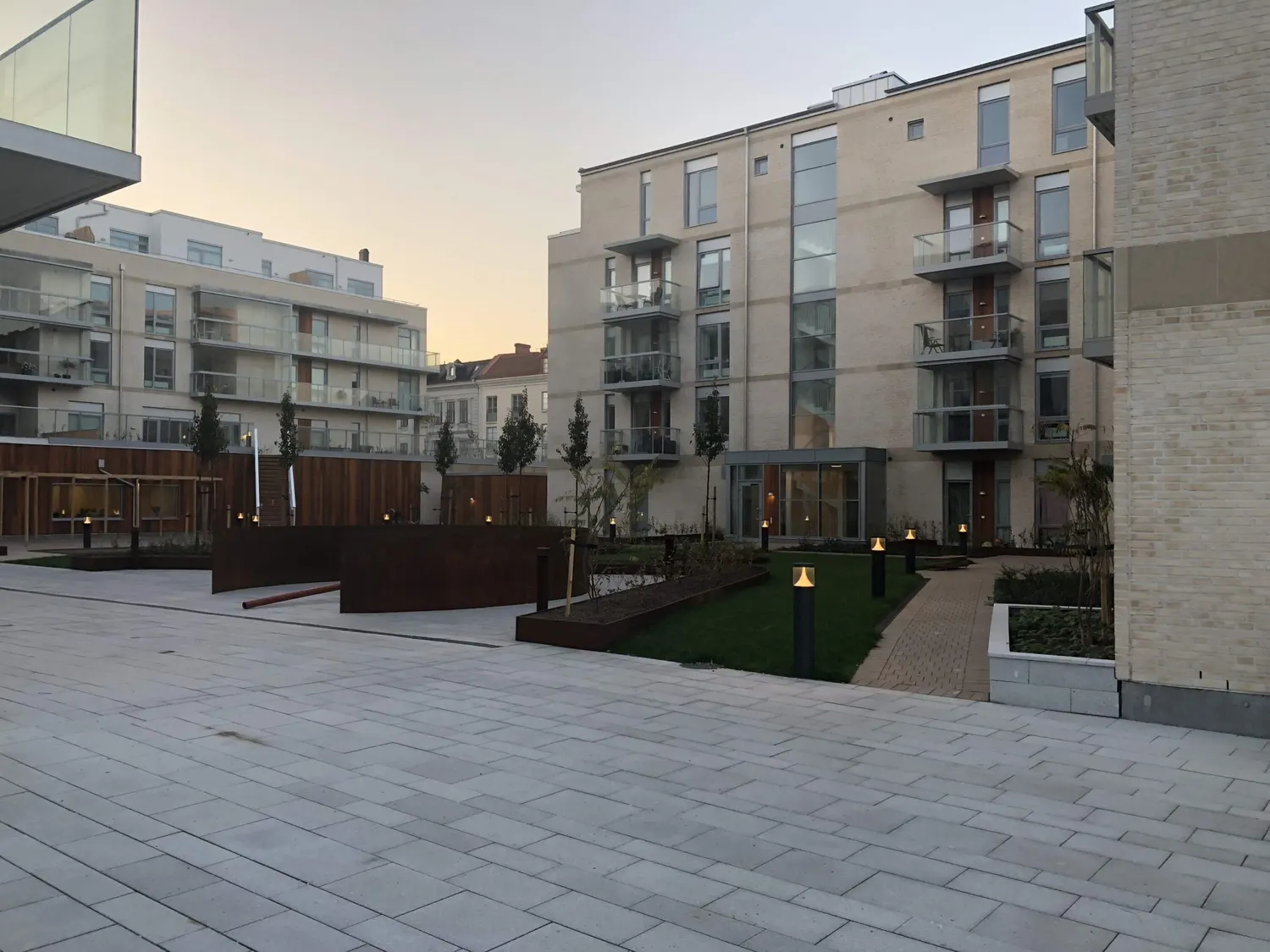 Innergården i skymning med belysta bostadshus runt om. Bild 12 av 18