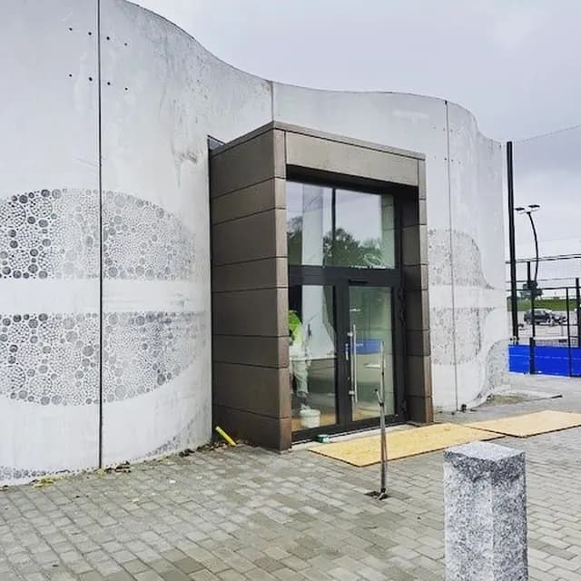 Entré infattad i bronsfärgad plåt i en svängd betongfasad. Bild 2 av 3